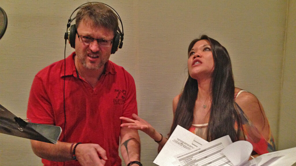 Steve Blum in the studio with another voice actor gesturing to script
