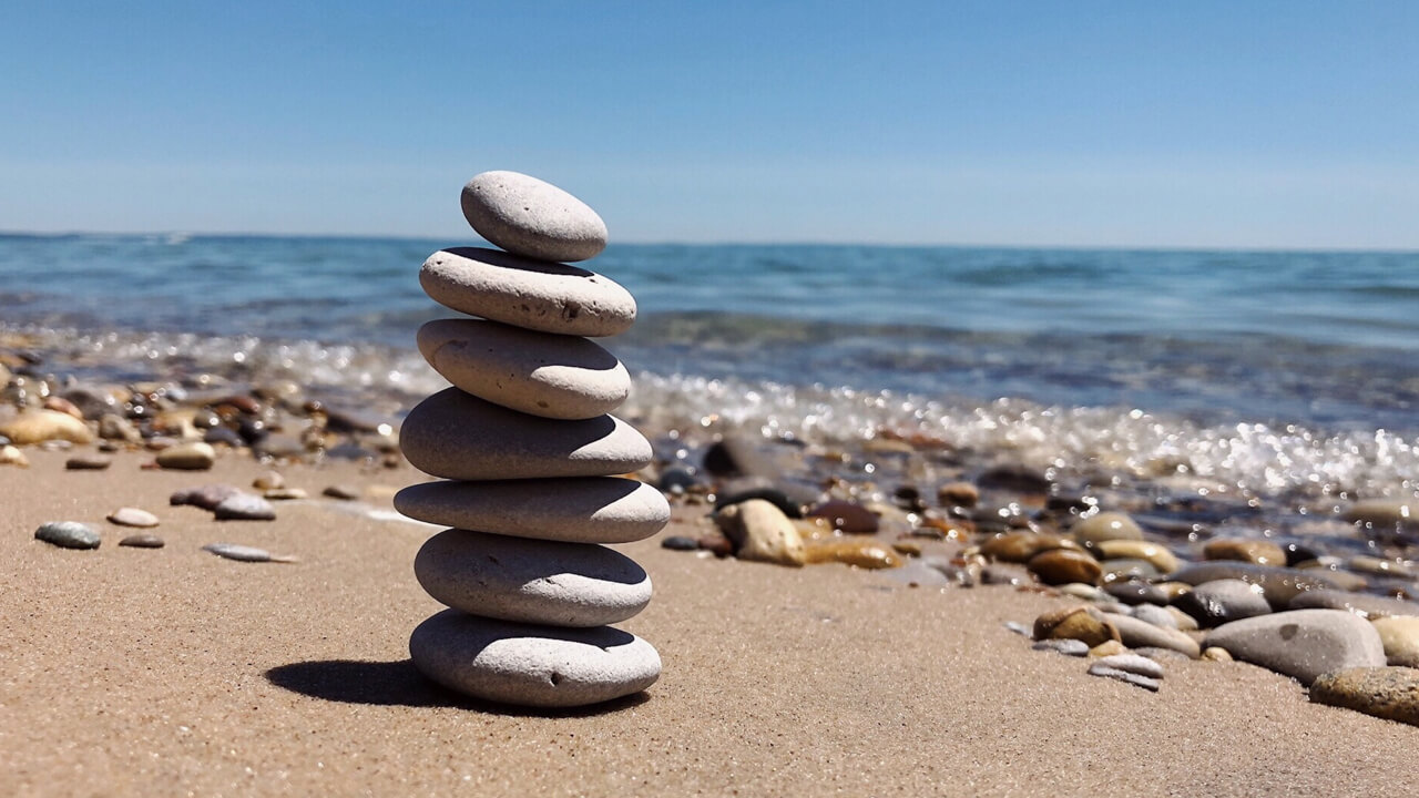 Image of 8 rocks of varying sizes stacked on top of eachother precariously on a beach