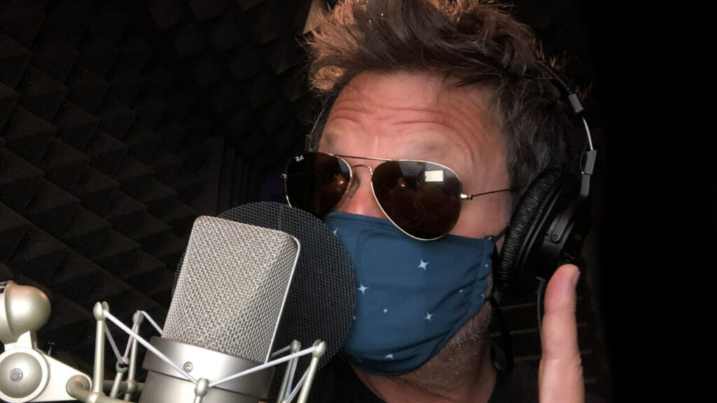 50 Classes-Beyond the Vision_Steve Blum at the mic with sunglasses and a mask on