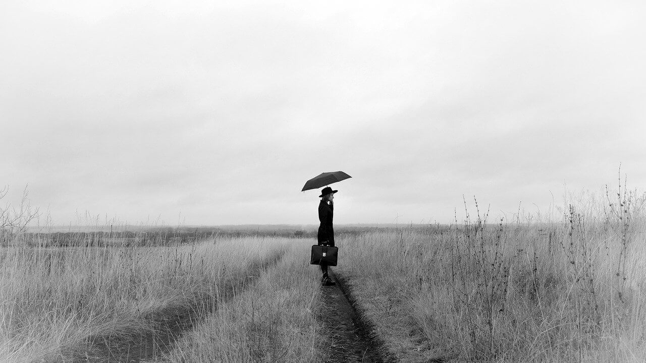 Black and white image of a woman with an umbrella standing in a field